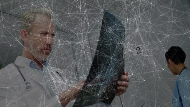 Male doctor raising X-ray to light, rotating and studying film for medical diagnosis, staff at desk