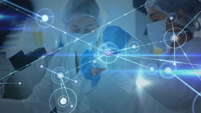 Two female lab techs lifting amber flask and analyzing sample, starting AR network over scope