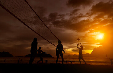 Young people playing beach volleyball by the ocean at sunset