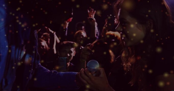 Host handing mic toward fan in music gig, inviting crowd singing while gold lights drifting