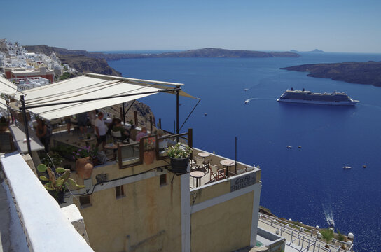 Modern cruiseship or cruise ship liner Equinox anchored in caldera of Santorini Island, Greece with harbor infrastructure and marine traffic panoramic city skyline view Mediterranean summer cruising
