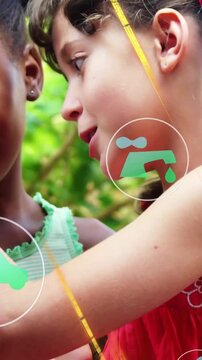 Vertical video: Girls leaning close, phone held up, learning environment topics from floating icons