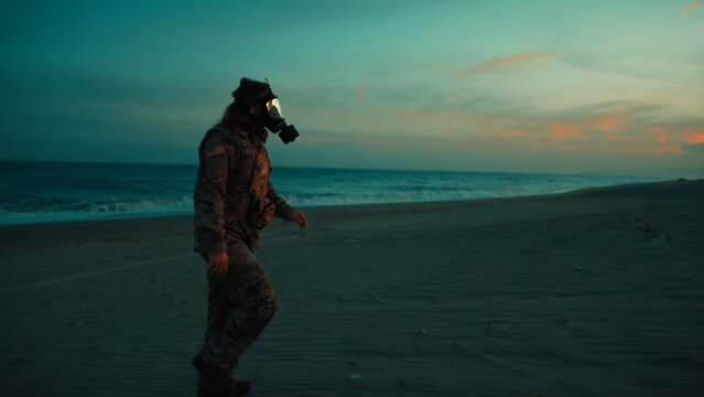 Soldier walks on beach contaminated by radiation from nuclear attack at sunset