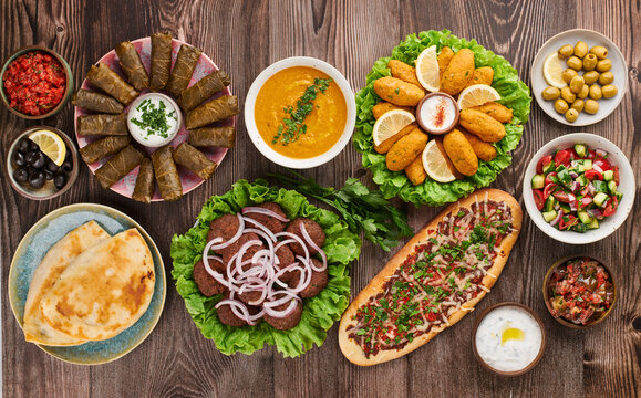Turkish cuisine flat lay with pide, kofte, lentil soup, mezze, dolma, salads, olives, yogurt dip and flatbread on table colorful traditional assortment