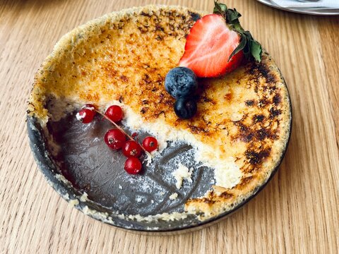 Close-up of creamy cr&egrave;me br&ucirc;l&eacute;e with burnt sugar crust and fresh berries, elegant dessert presentation, top view composition.