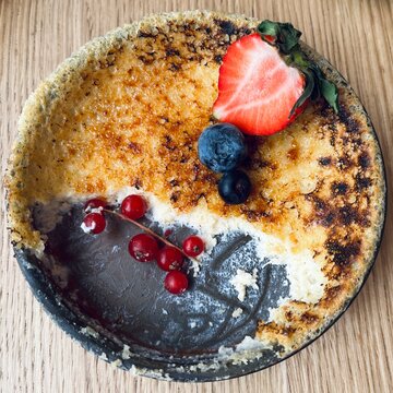 Delicious cr&egrave;me br&ucirc;l&eacute;e with golden caramel crust and berry garnish, creamy texture visible, stylish dessert on wooden background.