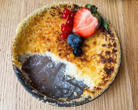 Homemade cr&egrave;me br&ucirc;l&eacute;e with crispy caramel top, decorated with strawberry, blueberries, and red currants, minimal food styling.