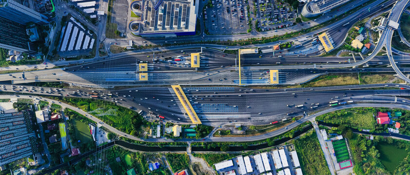 Aerial view of busy highway intersection in modern city during daytime, vehicles moving across multilane expressway with overpass structure, showcasing urban transportation.