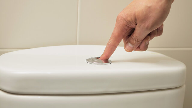 Close-up of male hand pushing a button to flush a close tool at home