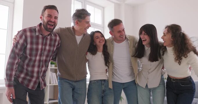 Happy young friends smiling together in a hug. Cheerful group of people laugh at camera at home, sharing unity, support, and friendship in a bright setting. Concept friendship, team, joy, together.