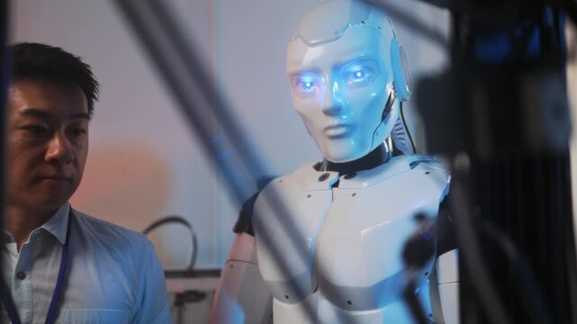 Technician observes robot activation scene, Asian technician views humanoid robot starting up in laboratory