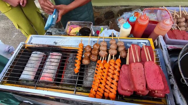 First-person video of street food: grilled sausages, grilled meatballs, and spam meat or canned processed meat skewered on bamboo skewers and grilled on a grill tray. Indonesian Street Food 4K