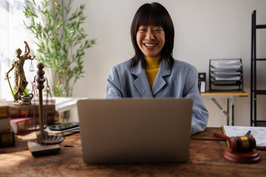 Asian female lawyer in suit at workplace with laptop, gavel and femida in office, Concepts of Law and Legal services.
