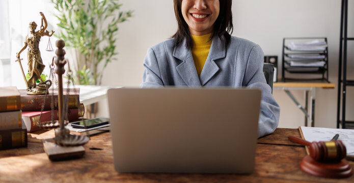 Asian female lawyer in suit at workplace with laptop, gavel and femida in office, Concepts of Law and Legal services.
