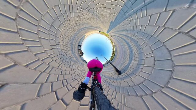 Cycling urban tiny planet, person riding bicycle on a sunny paved pathway with unique abstract visual effect, outdoor leisure activity