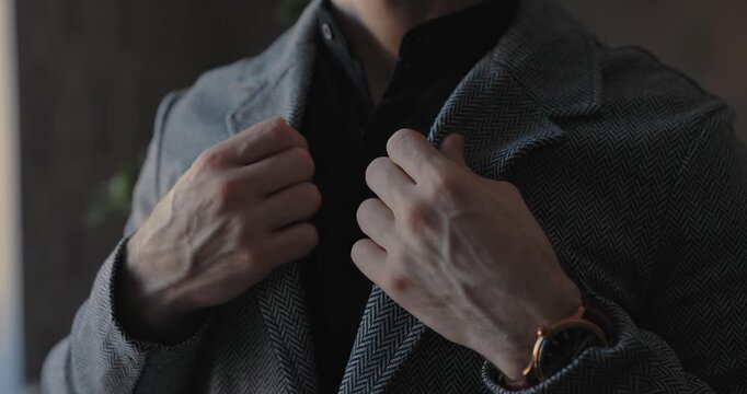 A man in a classic suit adjusts the collar of his jacket