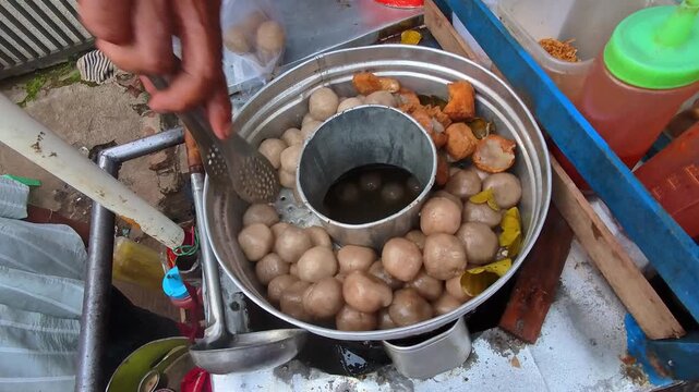 First-person video of a street food vendor's hand taking tapioca balls dumplings from a steaming pot. POV footage of a street food vendor serving a customer's order. Steady 4K resolution.