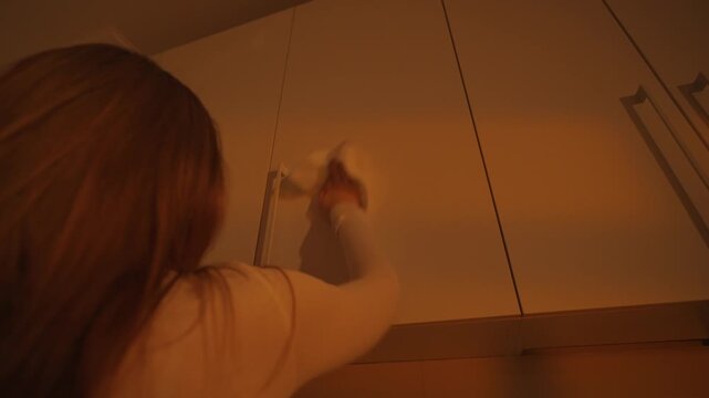 Low angle shot of woman cleaning white kitchen cabinet in warm light