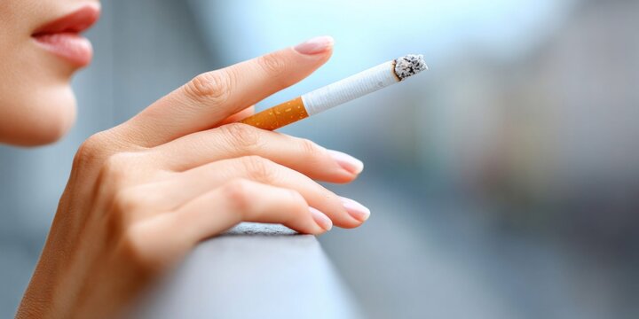 Close-up of a woman's hand holding a lit cigarette with ash and smoke