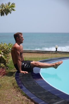 Athletic man performing L-sit exercise near pool with ocean view