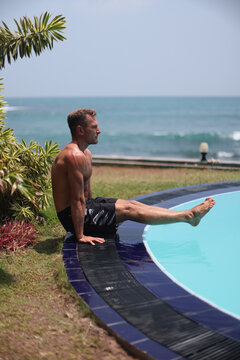 Athletic man performing L-sit exercise near pool with ocean view