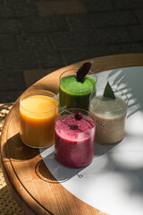 Fototapeta premium Variety of fresh fruit and vegetable smoothies served in glass cups on table in cafe setting