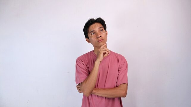 Asian young man gestures holding chin and looking up thinking about something