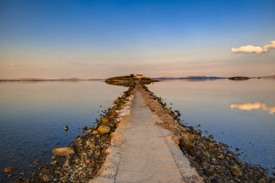 Lemnos Nea Koutali Saint Nicolas islet, Serene water reflecting blue and orange sky, connecting the mainland to a small island under a peaceful twilight