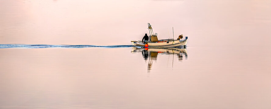 Lemnos, Fisher on a small boat creating a ripple wake on the mirror-like water, reflecting the soft sunrise colors. Solitude and journey concept