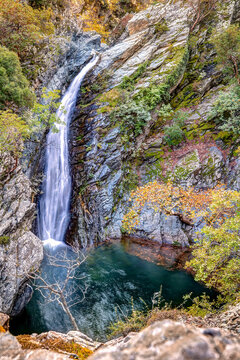 Samothraki Fonia Gorge. Waterfall cascading into a deep natural pool surrounded by autumn foliage and ancient rocks.