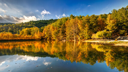 Obraz premium Thasos island, North Greece, Dam Maries. Lake reflecting vibrant autumn colors with hills and blue sky.