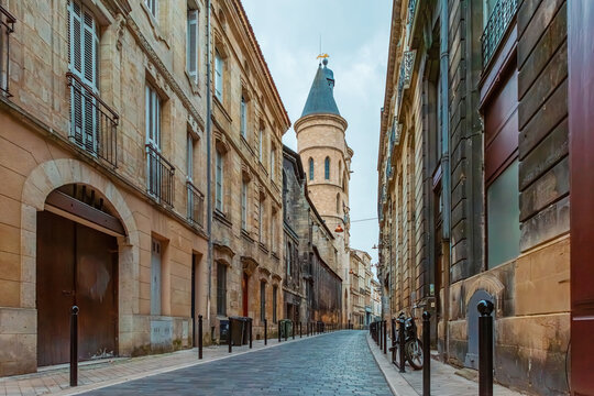 Historic street with stone buildings and narrow cobblestone road leading to Grosse Cloche medieval city gate with spires and bell tower in Bordeaux city center, Gironde, Nouvelle-Aquitaine, France