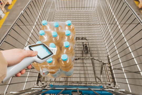 Person scanning barcode on plastic water bottle pack in shopping cart with mobile terminal
