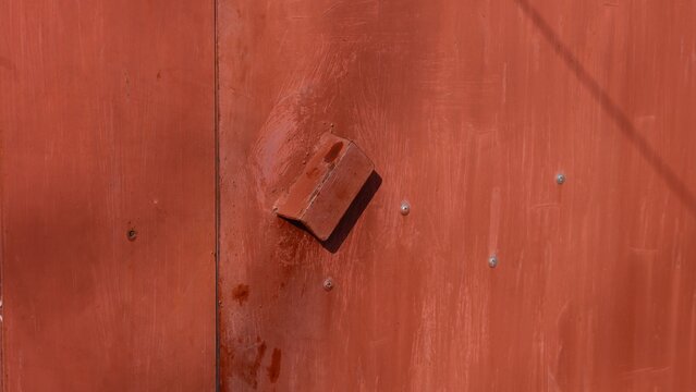 Close-up of a weathered red metal garage door with a welded handle and visible bolts.