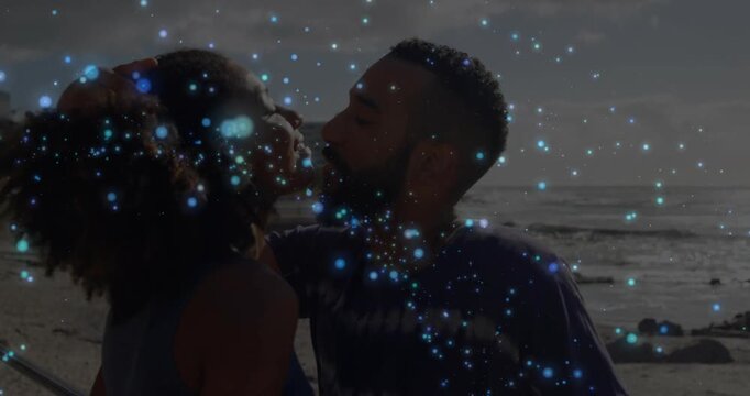 Man raising hand cupping woman head sharing kiss on beach affectionately as sparkle overlay moves