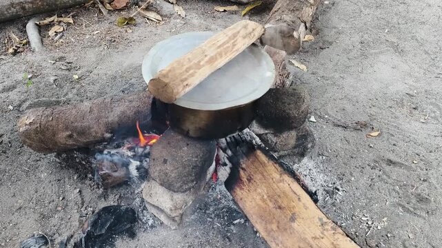 A pot sits on a makeshift campfire in a natural outdoor setting with wood.