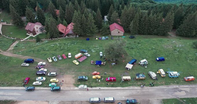 Breathtaking aerial view capturing an organized gathering of vintage cars and vans in a lush mountain setting