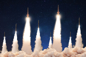 Naklejka premium diverse ballistic missiles being launched simultaneously at night under a starry sky, depicting a strategic missile strike scenario involving Iran, with massive plumes of smoke and light. War