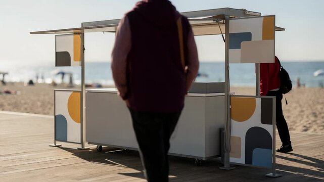 Popup food stall setup on a sunny beach boardwalk featuring a streamlined portable counter and branded signage with sand and sea out of focus behind.