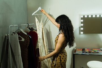 Model selecting clothing from a garment rack, preparing for a fashion show backstage with a vanity mirror