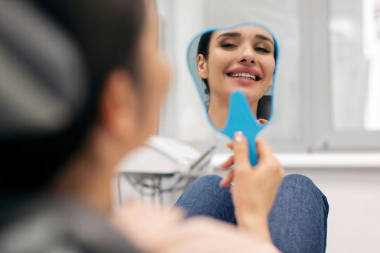 Happy woman looking at her reflection in small mirror after having dental treatment done at clinic