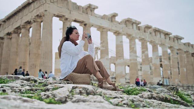 Tourist capturing photographic moments near the historic Parthenon in Athens, Greece using vintage camera