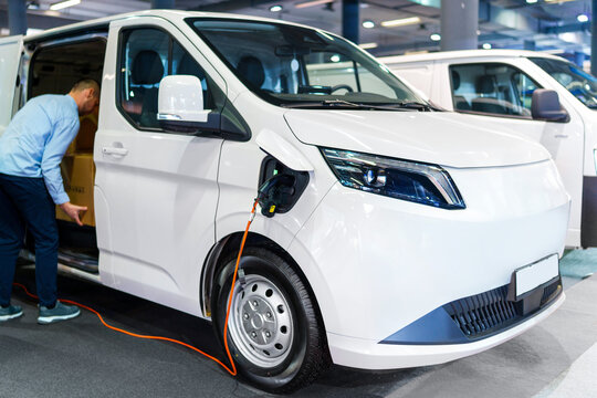 A courier removing packages from the modern electric van. The vehicle is plugged into a charging point