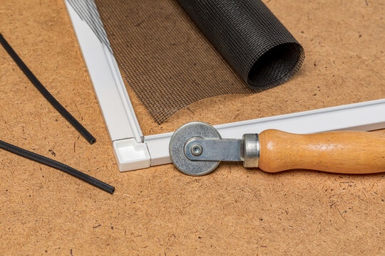Repairing window screen frame with new fiberglass mesh. Home repair, maintenance, and insect control concept.