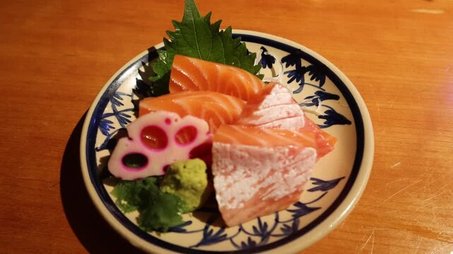 zooming in of close up of four slices of raw fresh salmon tummy sashimi with wasabi on the side on a Japanese pattern plate on a wooden table with copy space