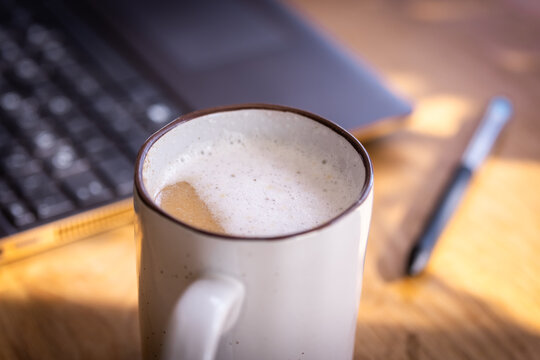 Frischer Kaffee mit etwas Milchschaum, im Hintergrund ist ein Laptop und ein Stift zu sehen