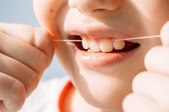 Close up child flossing teeth with dental floss string, oral hygiene and prevention concept.
