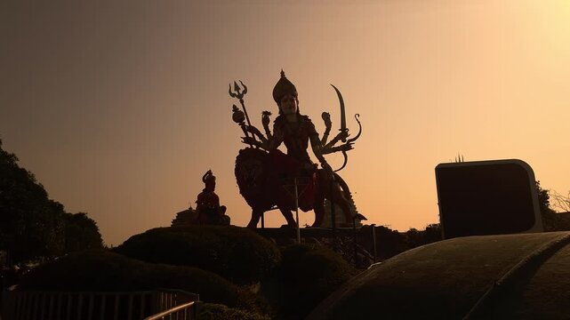 Big Goddess Durga statue at sunset in Chaar Dham Temple in Vrindavan, Uttar Pradesh India. Dramatic spiritual scene, golden sky, temple ambiance, ideal for religion, culture, and festival themes.