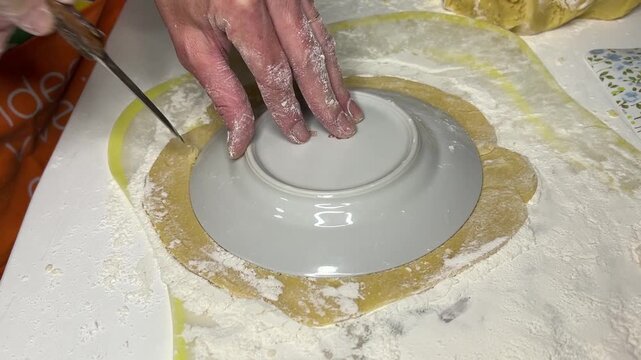 Horizontal side angle video: placing a bowl on rolled-out dough, cutting around it, removing excess, creating a round dough shape