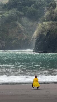 Woman in yellow jacket taking photos on Seixal black sand beach, Madeira Island, Portugal